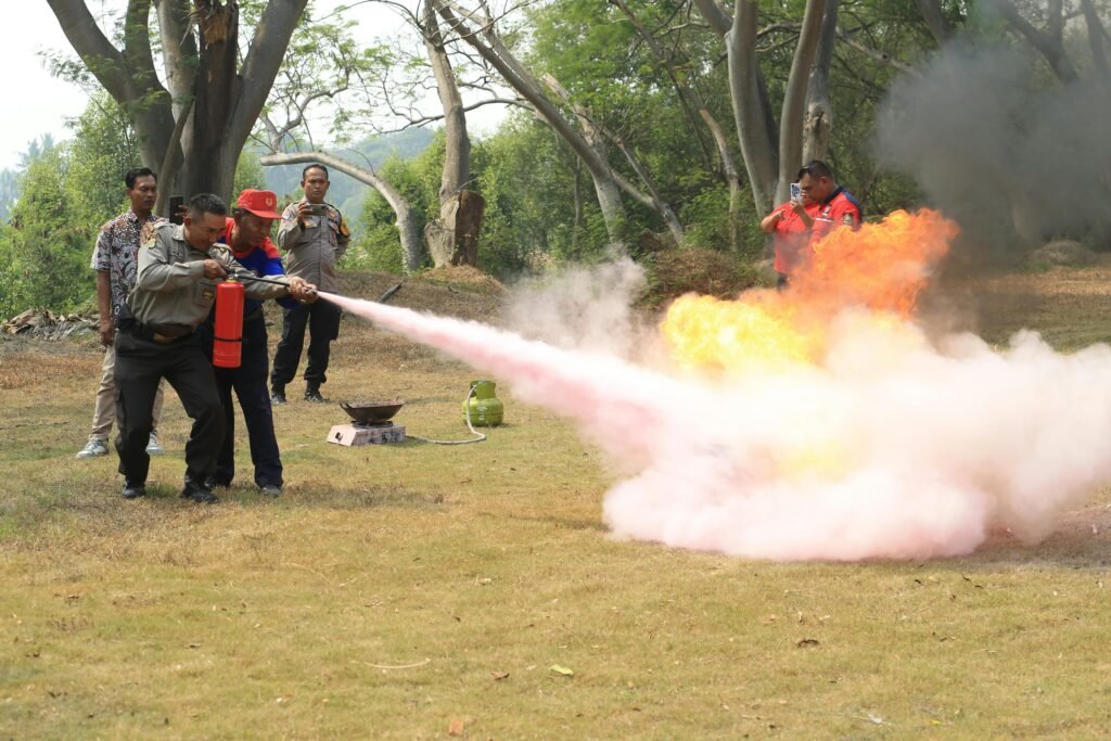 Fire safety training exercise with participants using a fire extinguisher in a rural outdoors setting.