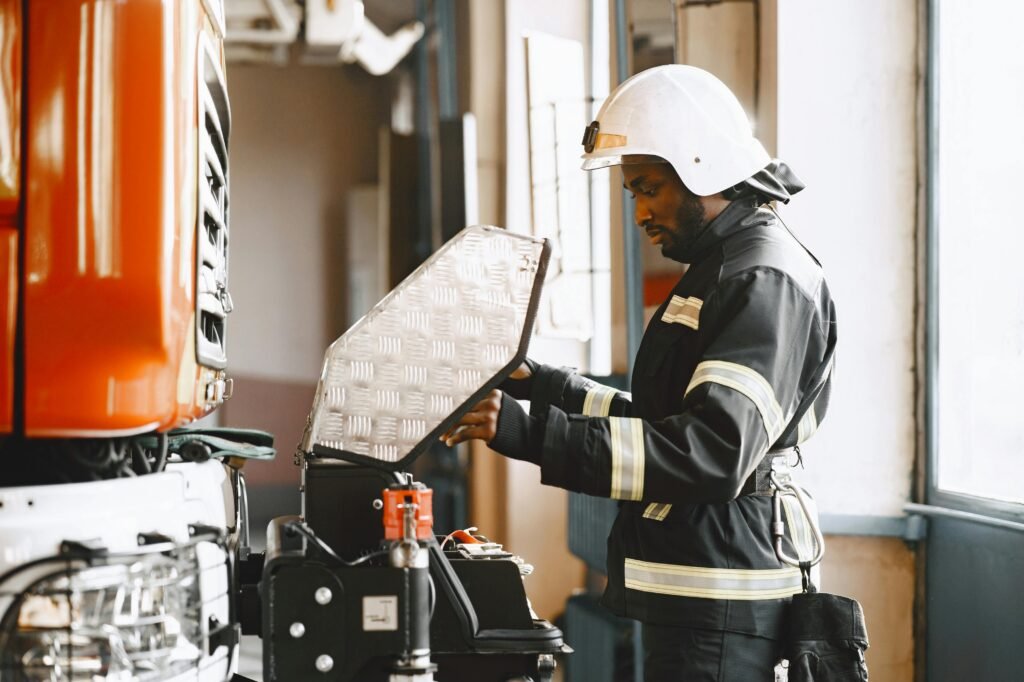 Firefighter in protective gear conducting maintenance on a fire truck indoors.